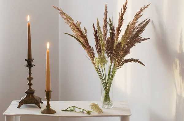 Ramo de flores silvestres y velas ardientes a la luz del sol en blanco i —  Fotos de Stock