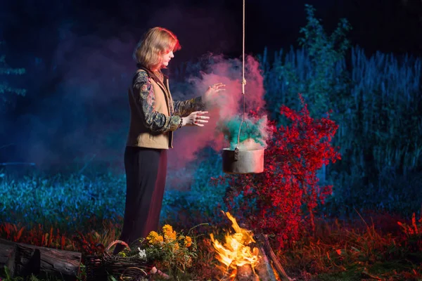 Young witch by  fire in night forest prepares  magic potion — Stock Photo, Image