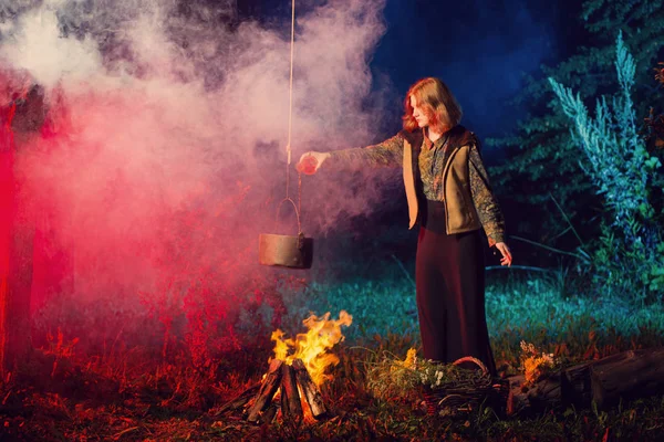 Jeune sorcière par le feu dans la forêt nocturne prépare potion magique — Photo