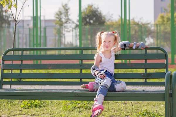 Bambina seduta sulla panchina nel parco giochi in pattini a rotelle — Foto Stock