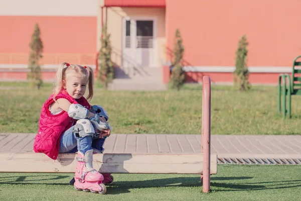 Bambina seduta sulla panchina nel parco giochi in pattini a rotelle — Foto Stock