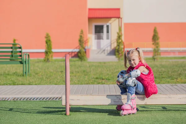 Klein meisje zittend op Bench in speeltuin in rolschaatsen — Stockfoto