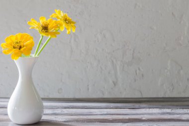 ahşap masa üzerinde beyaz vazo sarı zinnia 