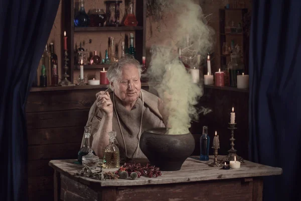 Elderly alchemist monk brews  magic potion — Stock Photo, Image