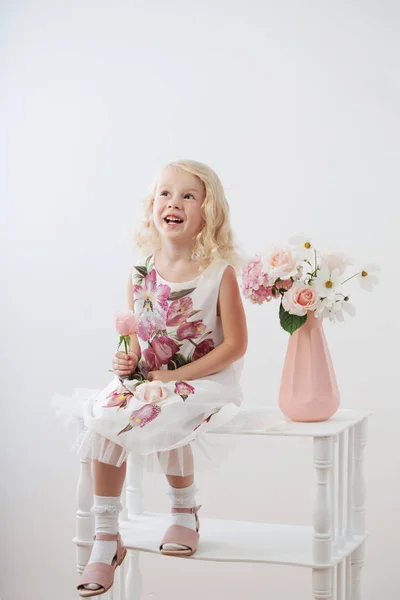 Mooie kleine blonde meisjes met bloemen op witte achtergrond — Stockfoto