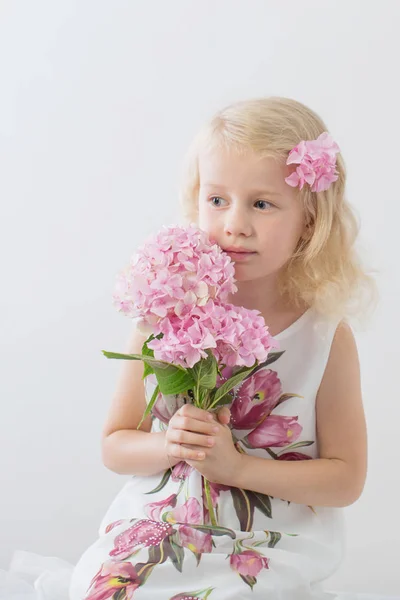 白いバックグロにピンクの花を持つ美しい小さなブロンドの女の子 — ストック写真