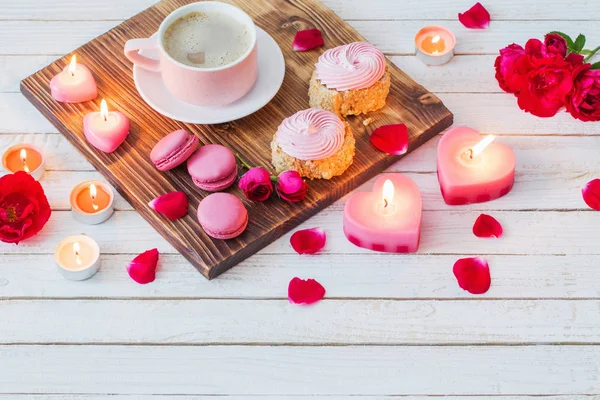 Чашка кофе с тортами, свечами и розами на белой деревянной спине — стоковое фото