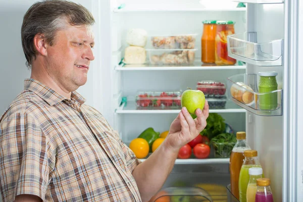 Зрелые мужчины в холодильнике с зеленым яблоком — стоковое фото