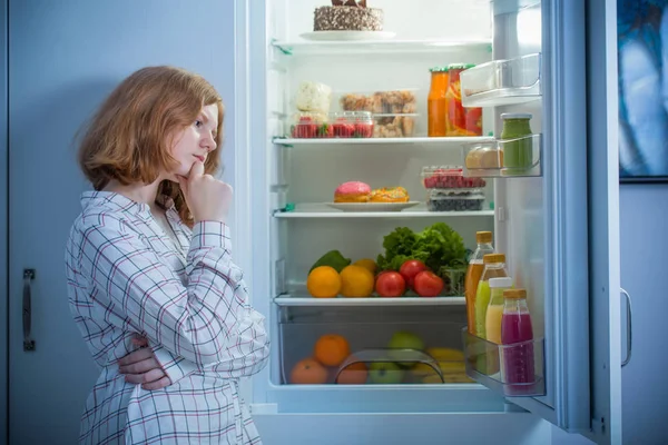 Tonårstjej i kylskåp med mat — Stockfoto