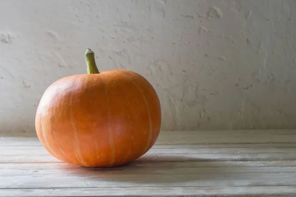 Zucca arancione su tavolo di legno su sfondo vecchio muro bianco — Foto Stock