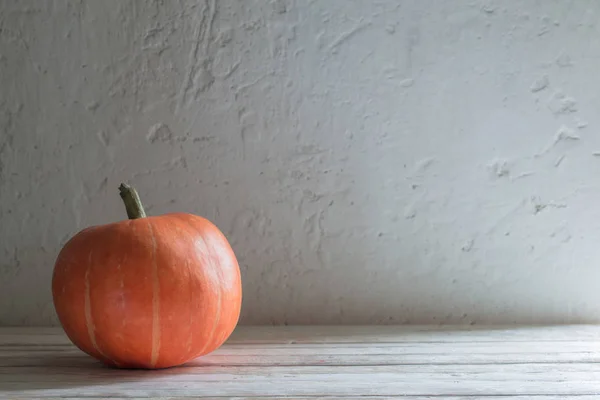 Orangefarbener Kürbis auf Holztisch vor Hintergrund alte weiße Wand — Stockfoto