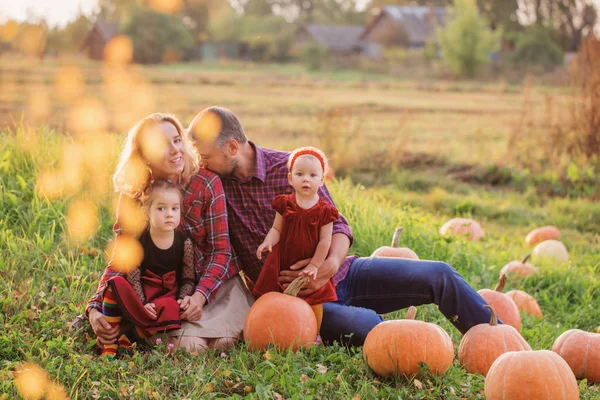 Šťastná rodina s oranžovými dýněmi na podzimním poli — Stock fotografie