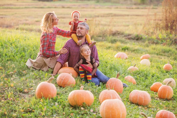 Família feliz com abóboras laranja no campo de outono — Fotografia de Stock