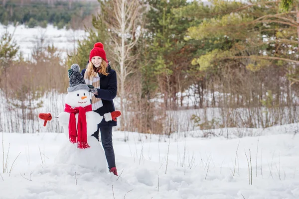 Счастливая девочка-подросток со снеговиком в зимнем лесу — стоковое фото