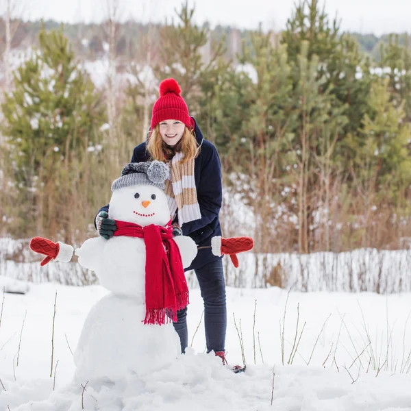 Щаслива дівчина-підліток зі сніговиком в зимовому лісі — стокове фото