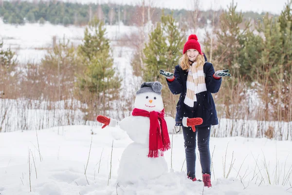 Lycklig tonåring flicka med snögubbe i vinter skog — Stockfoto