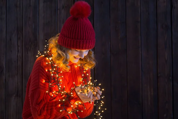 Meisje in rode hoed met kerst licht op houten achtergrond — Stockfoto