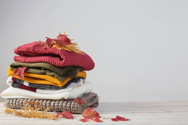 Pila de suéteres con hojas de otoño sobre mesa de madera blanca —  Fotos de Stock