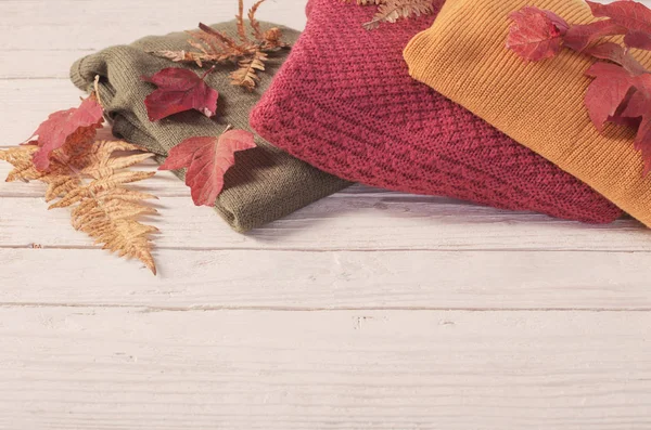 Stack of sweaters with autumn leaves  on  white wooden table — Stock Photo, Image