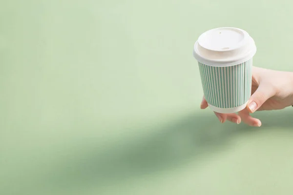disposable paper cup with coffee in women hand on green backgrou