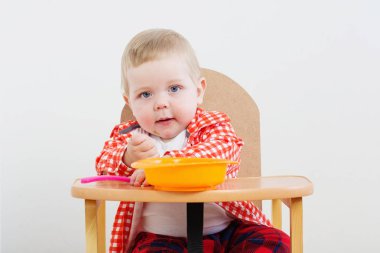 Arkadaki beyaz duvarda tabak ve kaşıkla küçük bir çocuk.