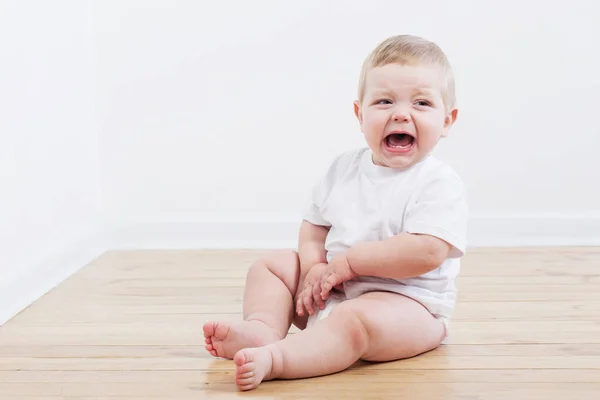 Bebê chorando sentado no chão de madeira — Fotografia de Stock