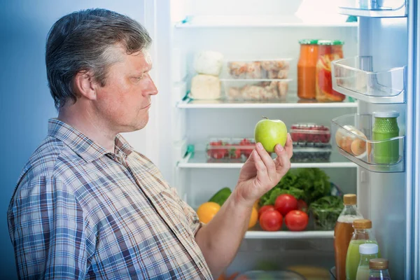 Volwassen mannen in de koelkast met groene appel — Stockfoto