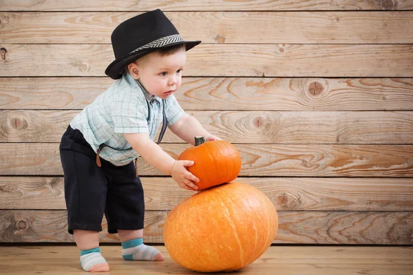 Baby in black hat with pumpkins on wooden background — Stock Photo, Image