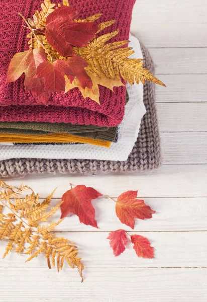 Hromada svetrů s podzimními listy na bílém dřevěném stole — Stock fotografie