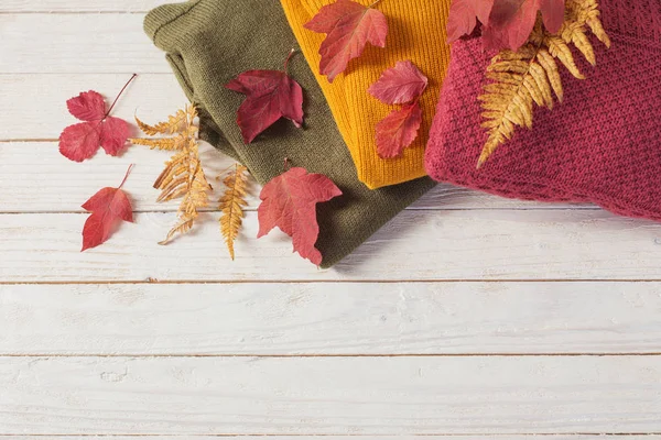 白い木のテーブルに秋の葉を持つセーターの山 — ストック写真