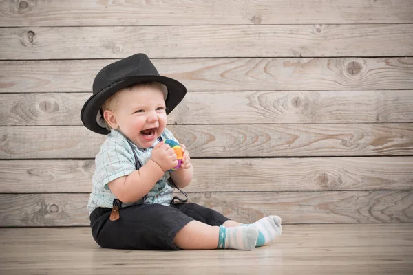 Bebé en sombrero negro, camisa y tirantes pantalones cortos en backgr de madera —  Fotos de Stock