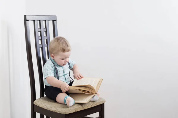 Baby med bok sitter på stol på vit bakgrund — Stockfoto