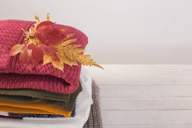 Sonbahar yapraklı kazak yığını beyaz ahşap masada.