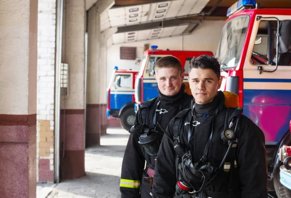 Bomberos jóvenes en el fondo de los camiones de bomberos —  Fotos de Stock
