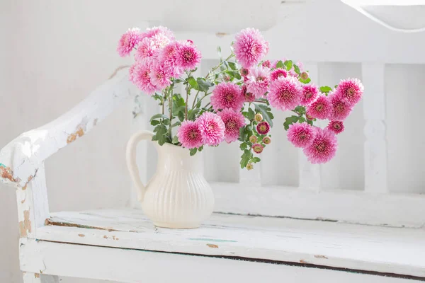Розовые хризантемы в кувшине на старой белой деревянной скамейке — стоковое фото