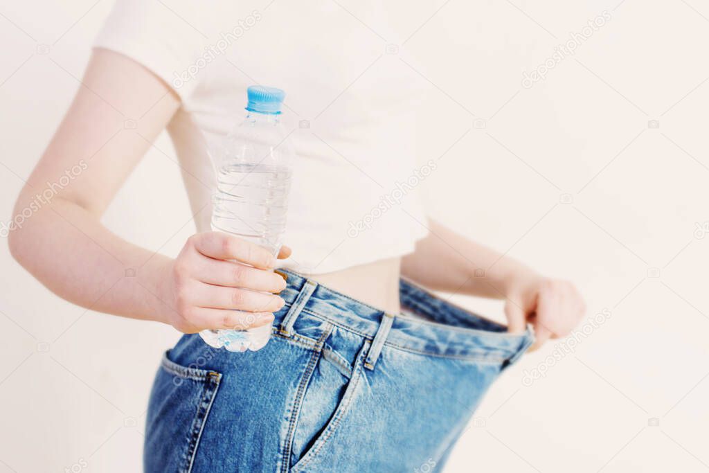 girl with water in bottle pulling her big jeans and showing weight loss