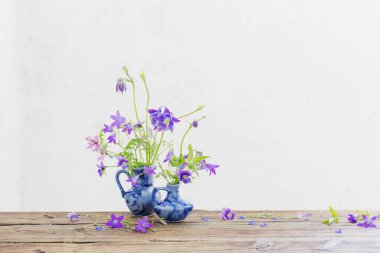 Eski ahşap masada mavi sürahi içinde yaz çiçekleri