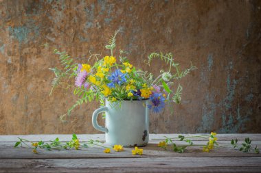 summer flowers in old cup on wooden background clipart