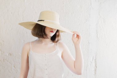 Arkadaki beyaz duvarda hasır şapkalı esmer kız.