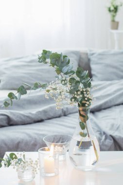 Beyaz yatak odasındaki cam vazoda yanan mumlar ve okaliptüsler.