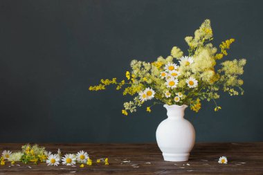 Beyaz vazodaki yabani çiçekler koyu arkaplanda