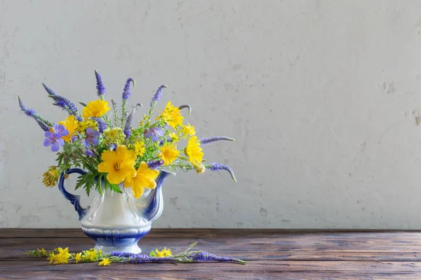 bouquet with blue and yellow flowers in teapot on wooden table
