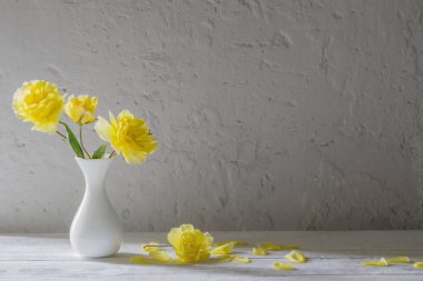 Beyaz vazodaki sarı güller arka plandaki beyaz duvarda