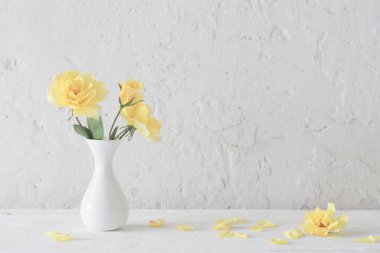 Beyaz vazodaki sarı güller arka plandaki beyaz duvarda