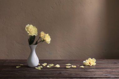 Arkaplan duvarında beyaz vazoda sarı güller