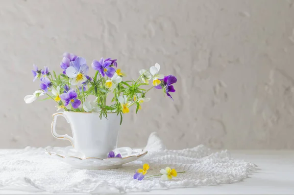 viola flowers in white cup on white background