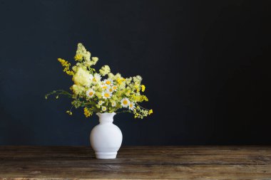 Beyaz vazodaki yabani çiçekler koyu arkaplanda