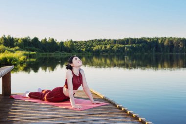 Yazın göl kenarındaki ahşap iskelede yoga yapan kız.