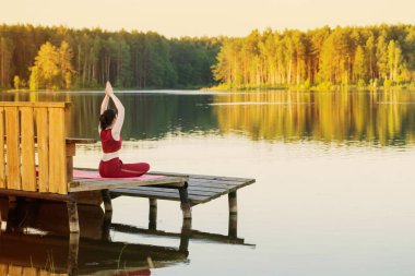Yazın göl kenarındaki ahşap iskelede yoga yapan kız.