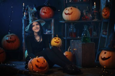 Cadılar Bayramı için dekorun arka planında balkabağı olan cadı gibi giyinmiş genç bir kız.